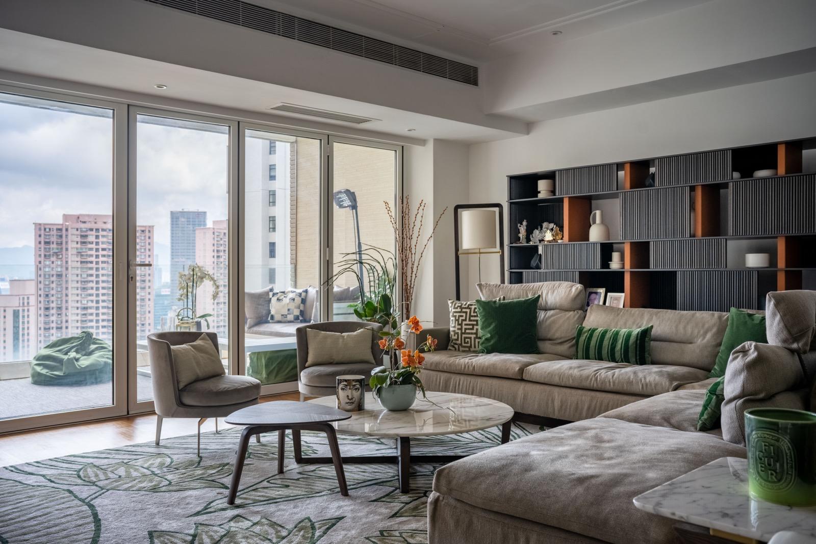 Wide living room with green armchairs, beige sofa, botanical rug and city views