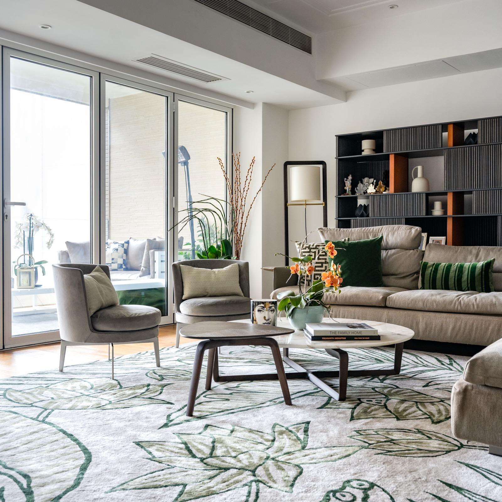 Green armchairs and beige sofa on a botanical rug beside balcony doors