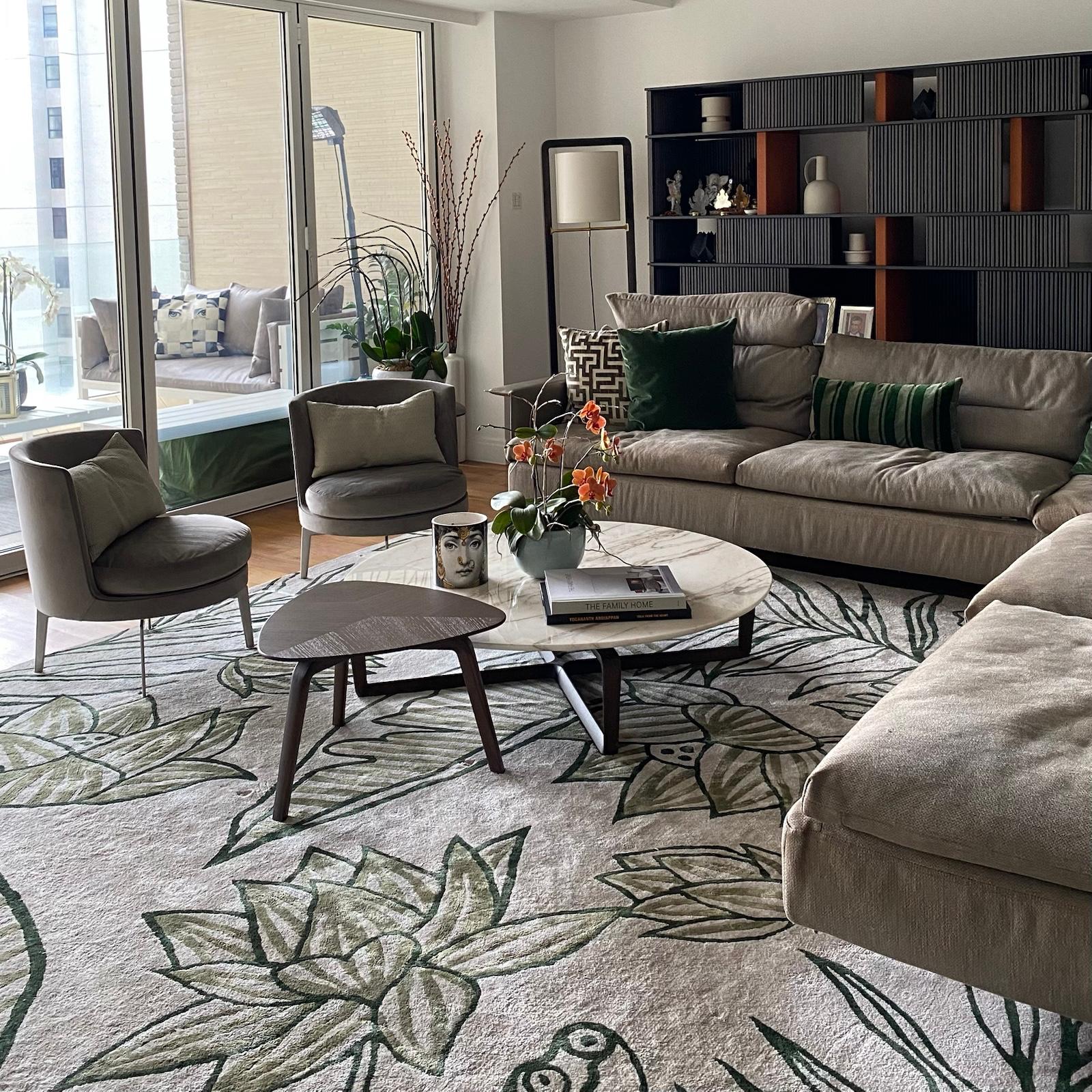 Living room with beige sectional, dark shelving and green armchairs beside balcony windows