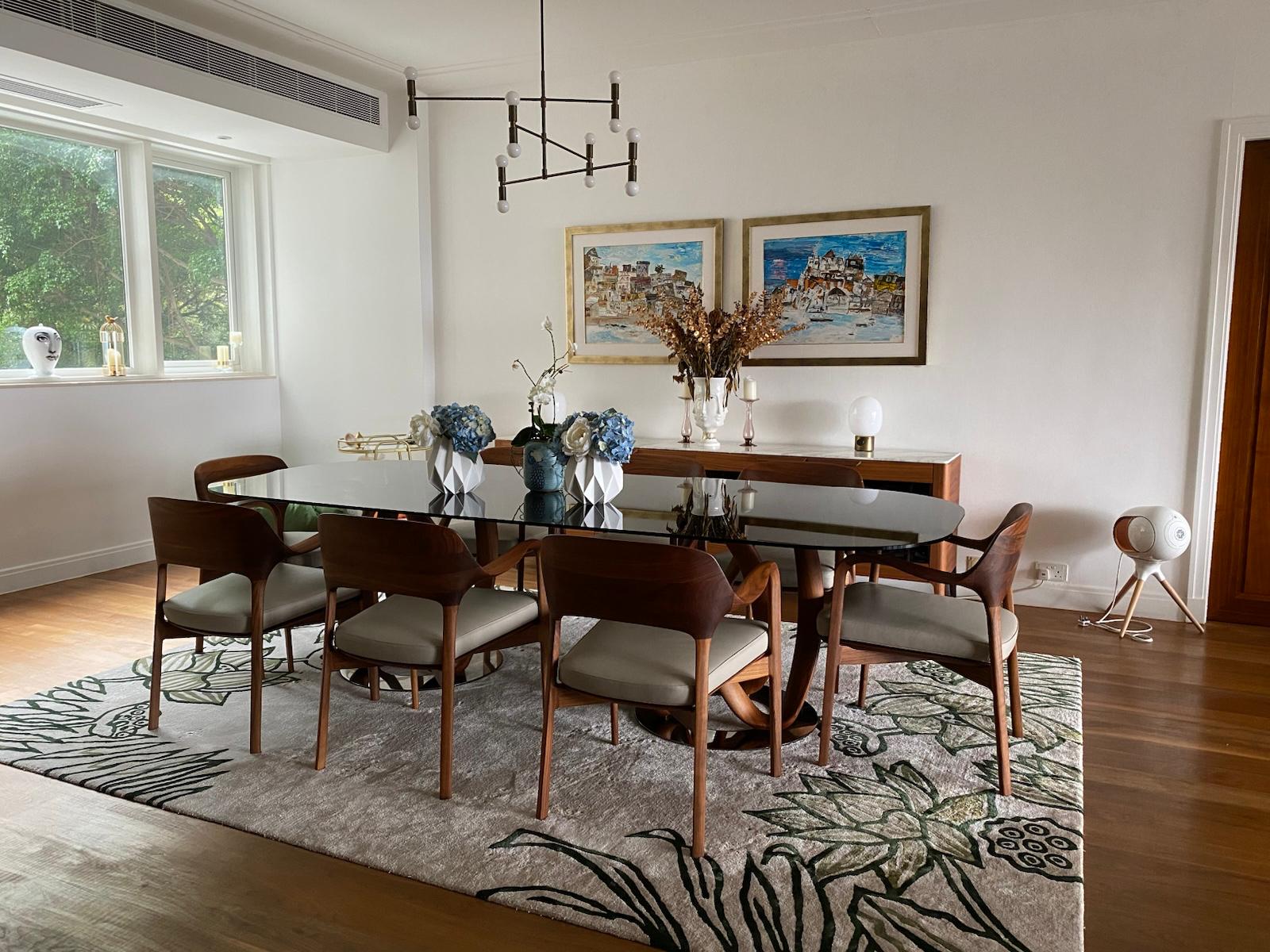 Dining table and timber chairs on a botanical rug beside a bright window