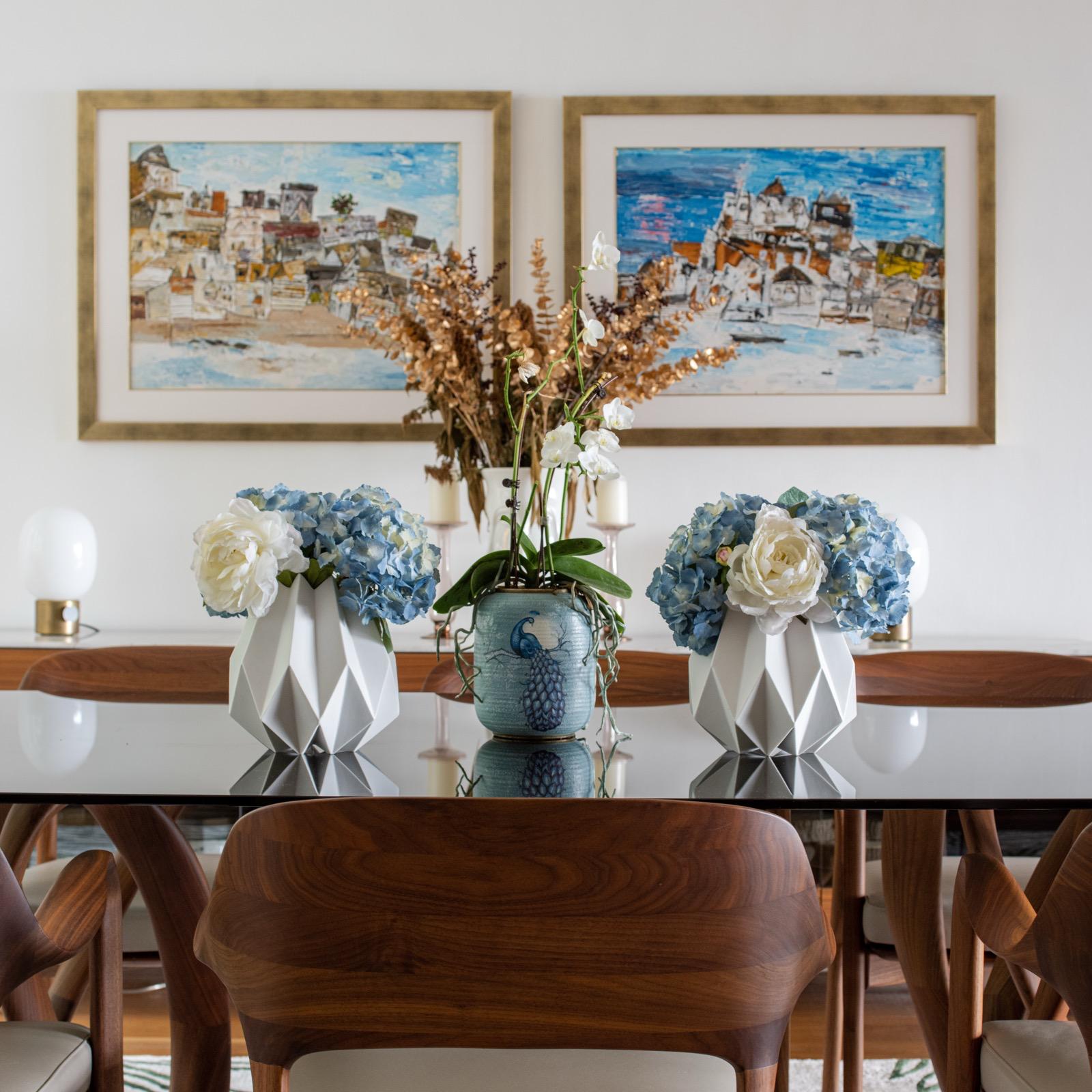 Blue and white floral arrangements on the dining table beneath paired artworks