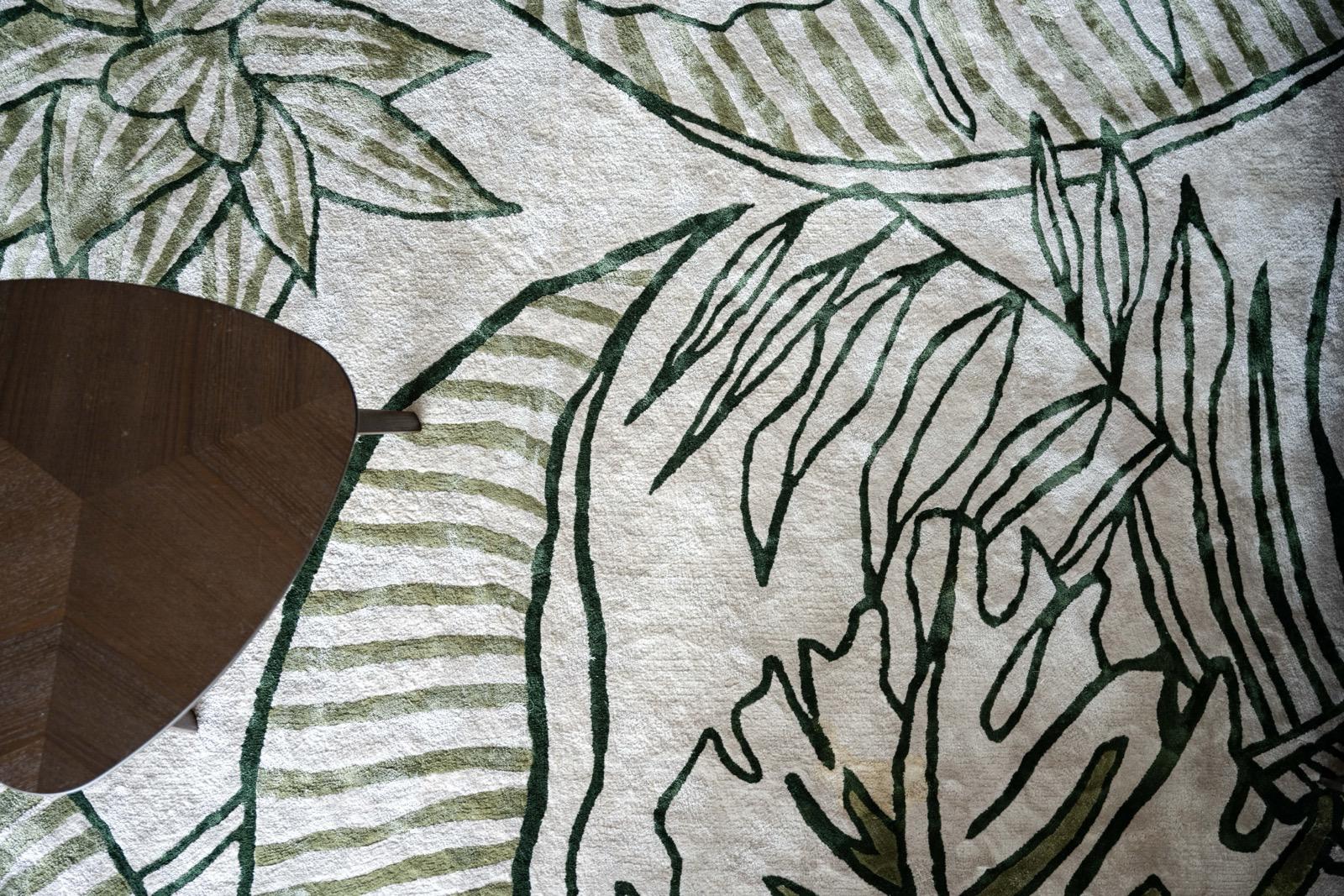 Detail of the botanical rug with green leaf outlines beside a dark coffee table
