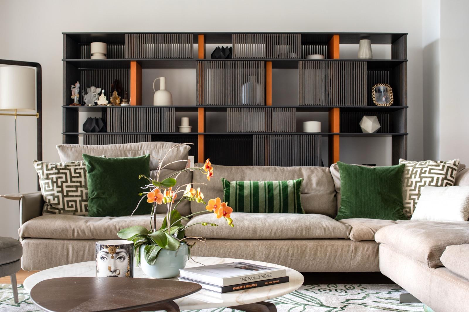 Beige sectional sofa with green cushions, an orange orchid and dark shelving with orange accents