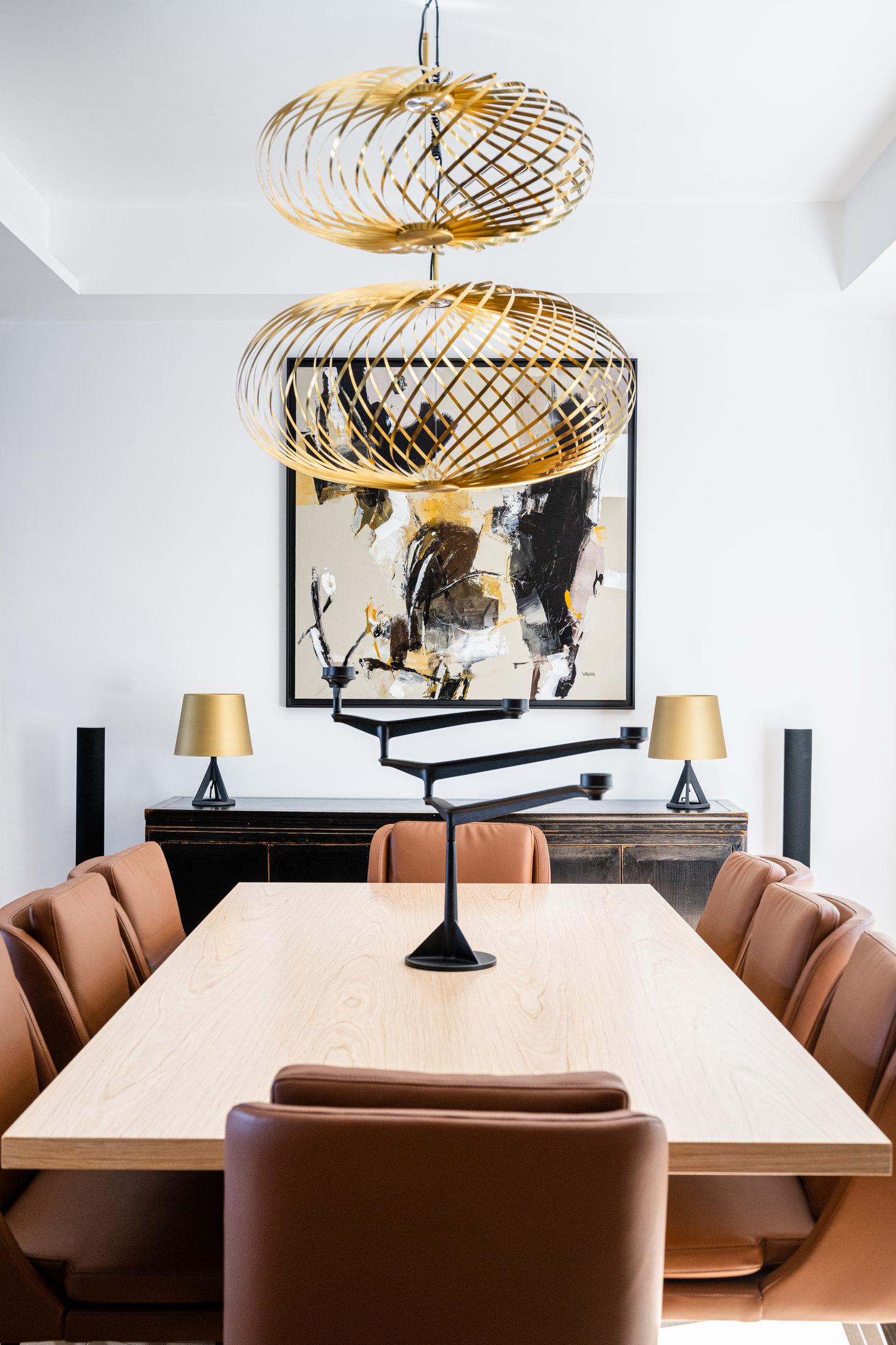 Dining table and upholstered chairs beneath sculptural woven gold pendant lights