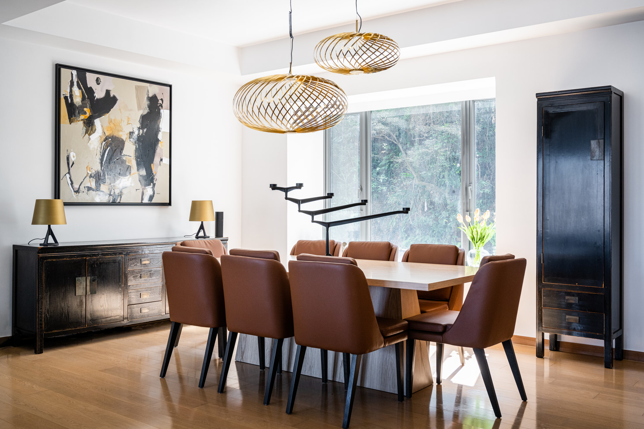 Timber dining table with rust chairs, gold pendant lights and abstract artwork above a dark sideboard