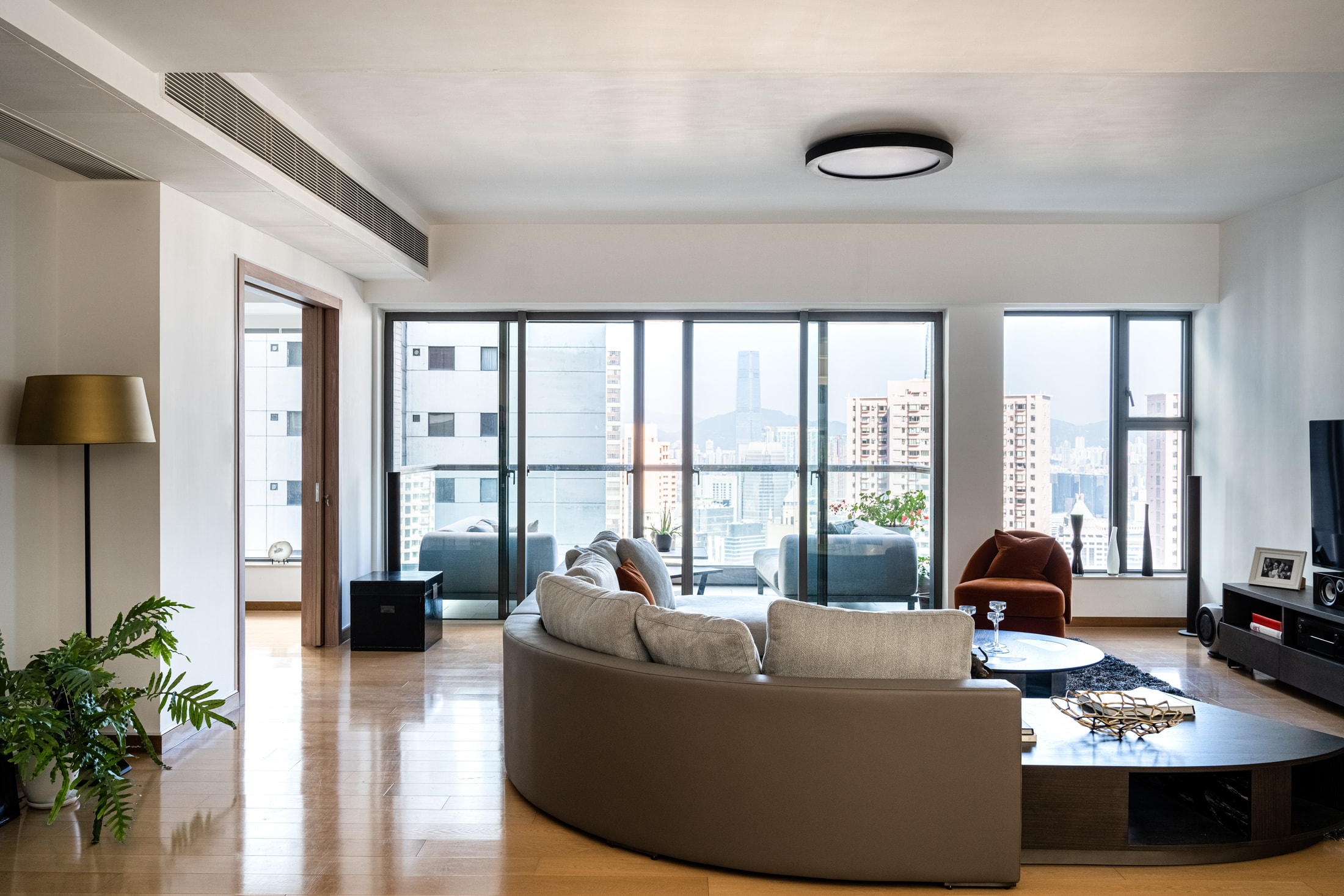 Open living room viewed from behind the curved sectional, with balcony windows and a rust armchair