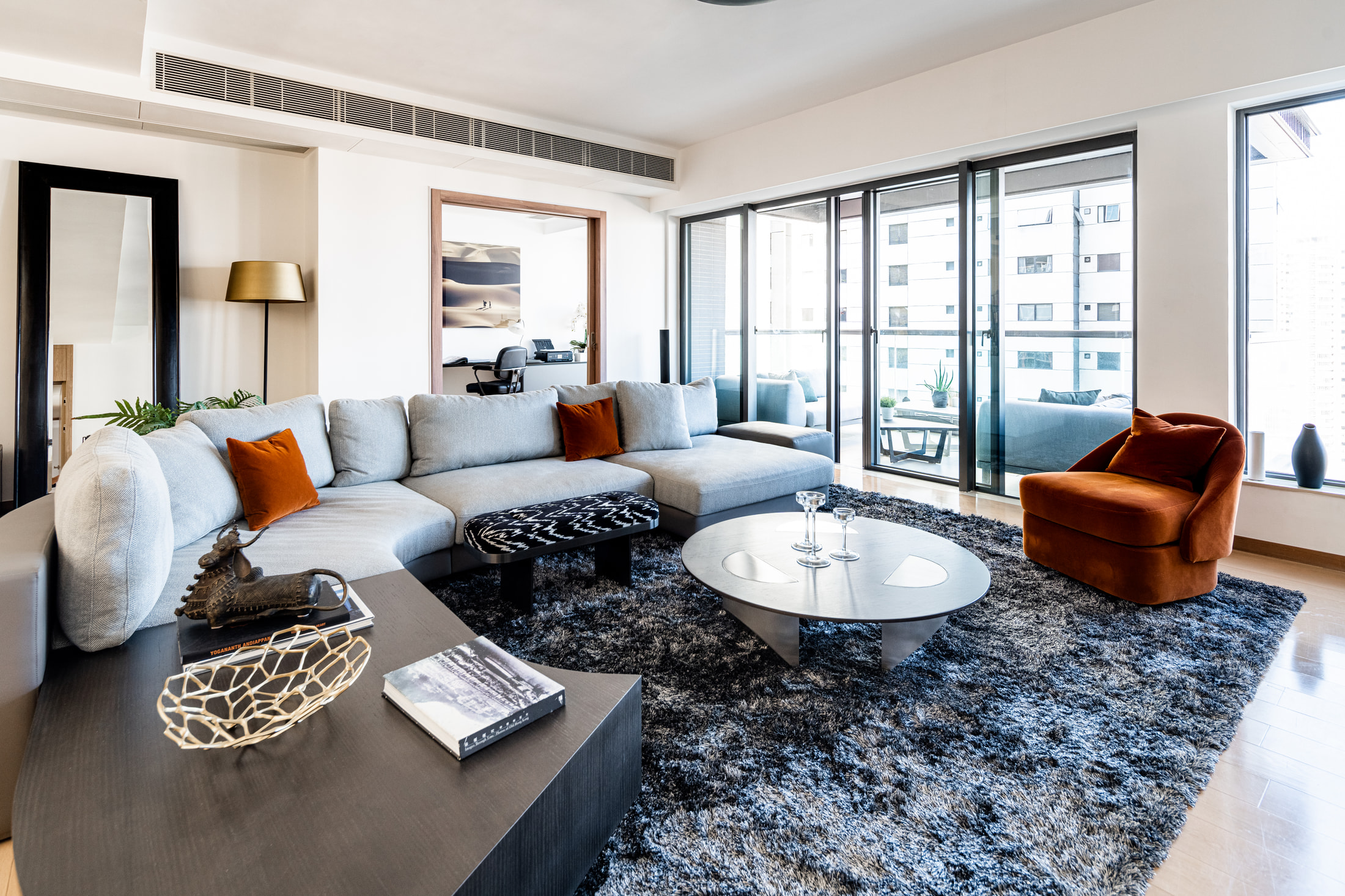 Grey sectional sofa, rust velvet armchair and oval coffee table beside balcony windows