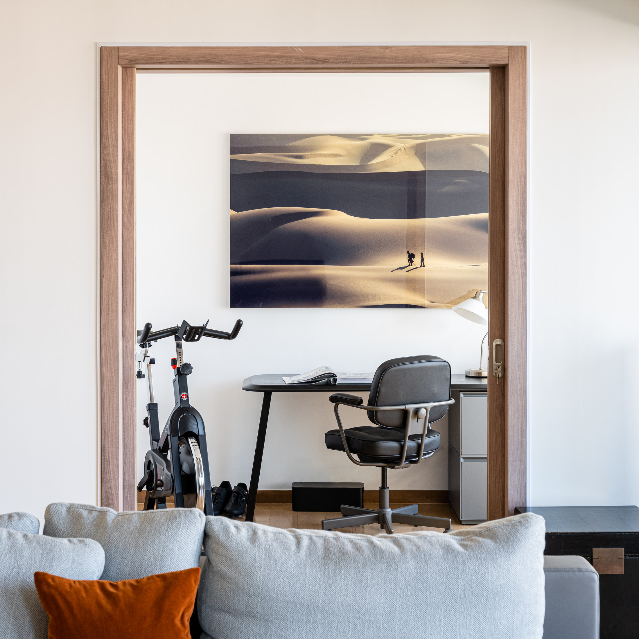 Home office with a black desk, ergonomic chair, bicycle and desert landscape artwork