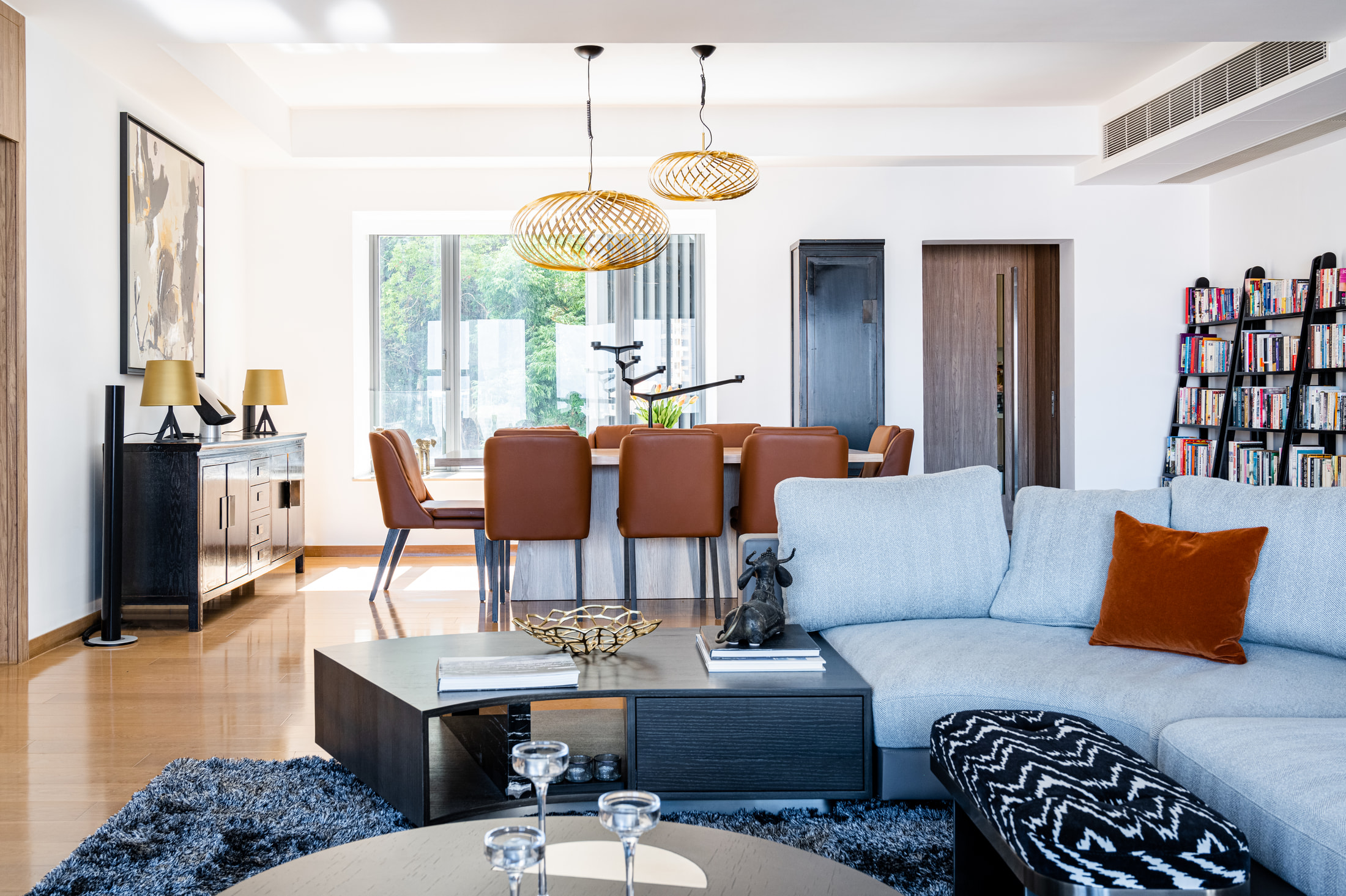 Living and dining spaces with a grey sofa, timber table and woven gold pendant lights