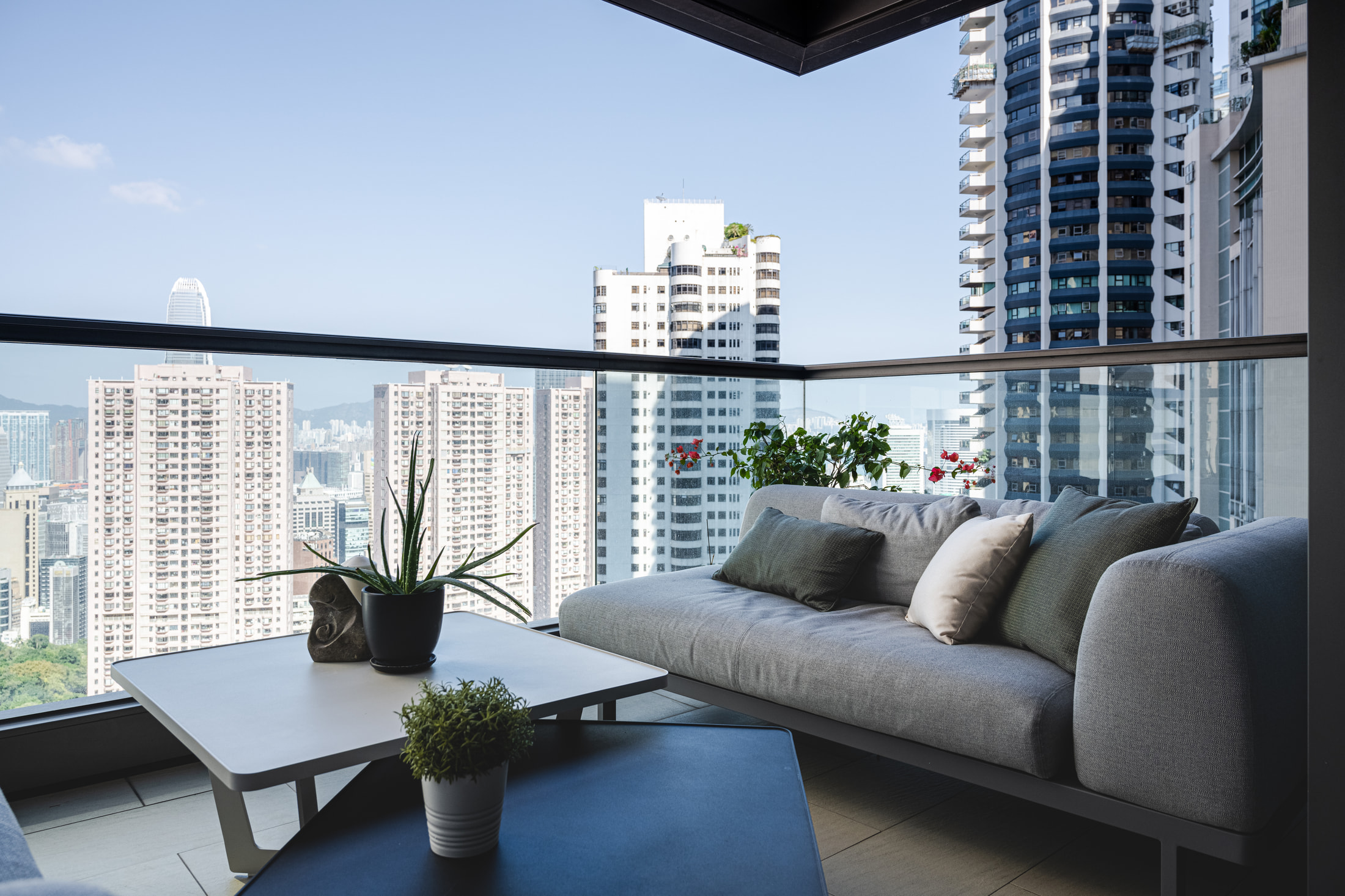 Balcony seating with a grey sofa, low tables, plants and a city view