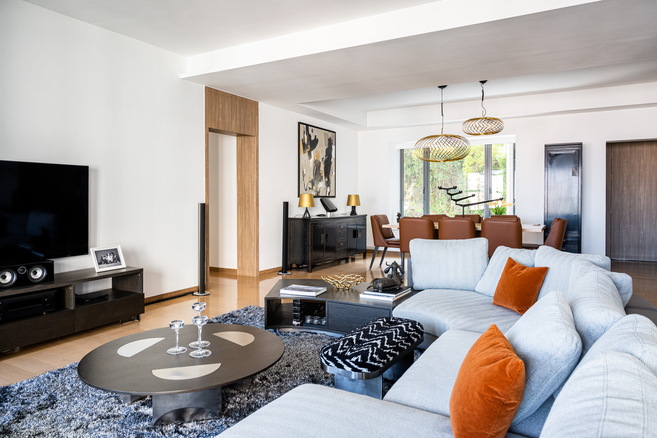 Grey sectional with rust cushions facing a dark television console beside the dining area