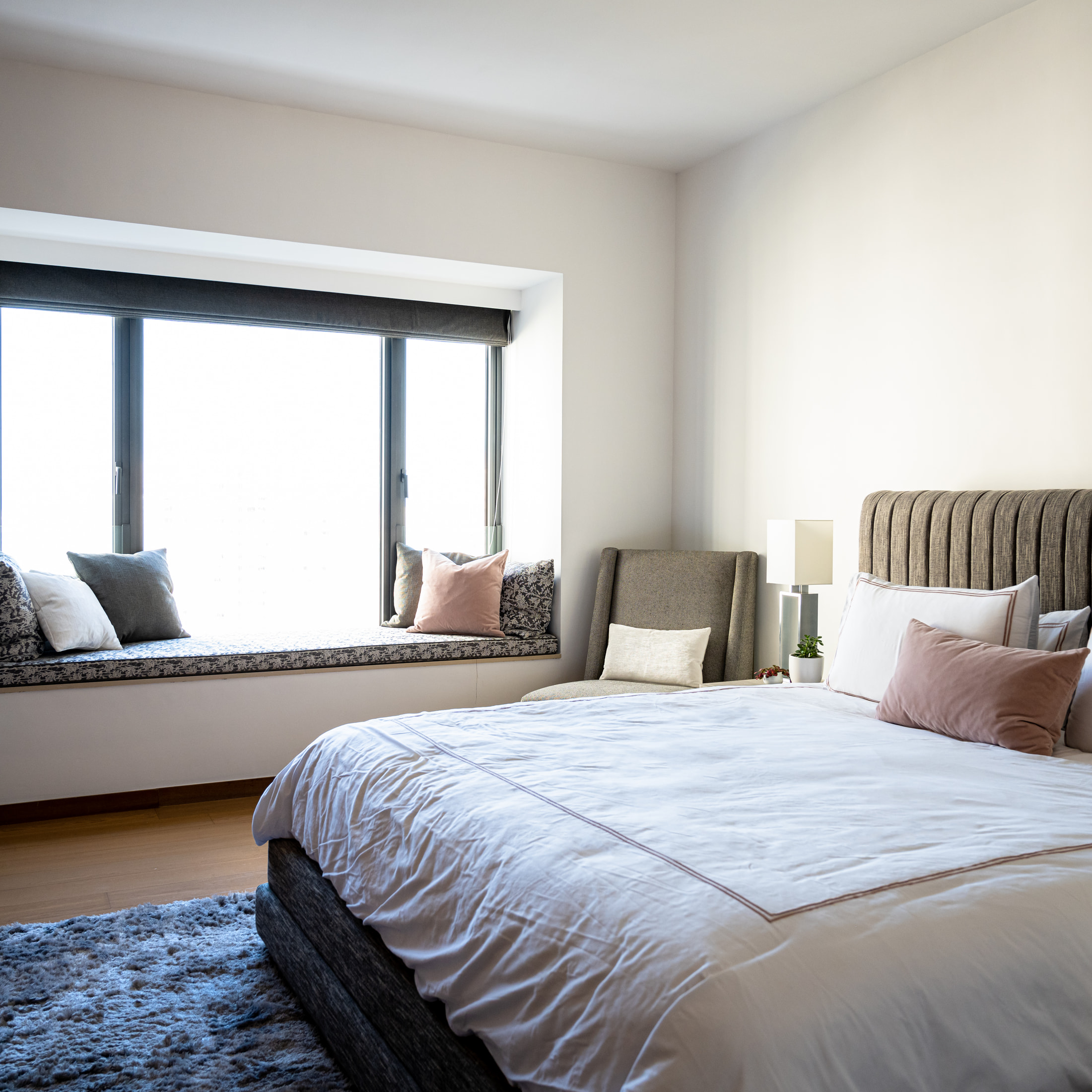 Bedroom with an upholstered headboard, soft bedding, patterned rug and window seat