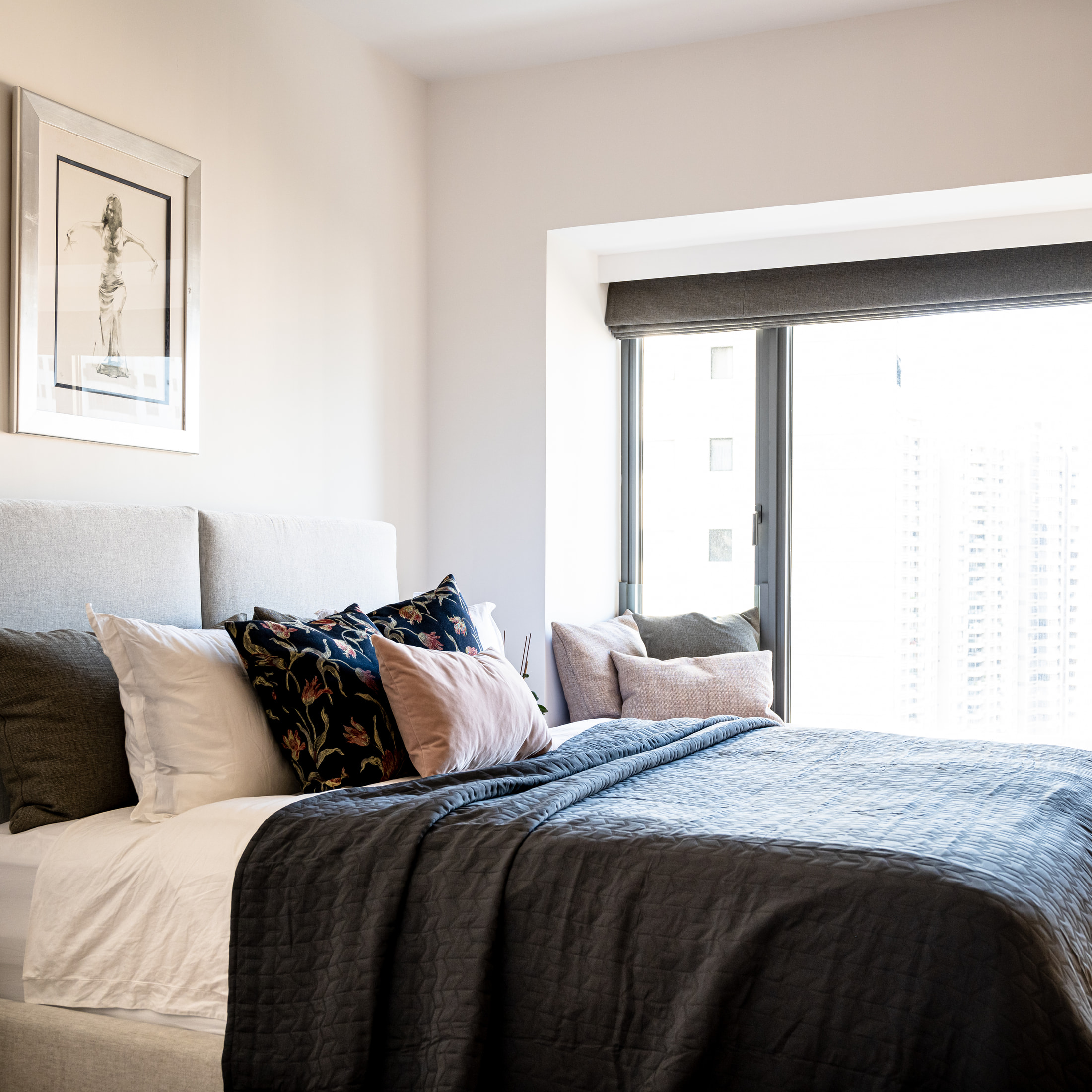 Bedroom with pale bedding, a dark throw and cushions beside a large window