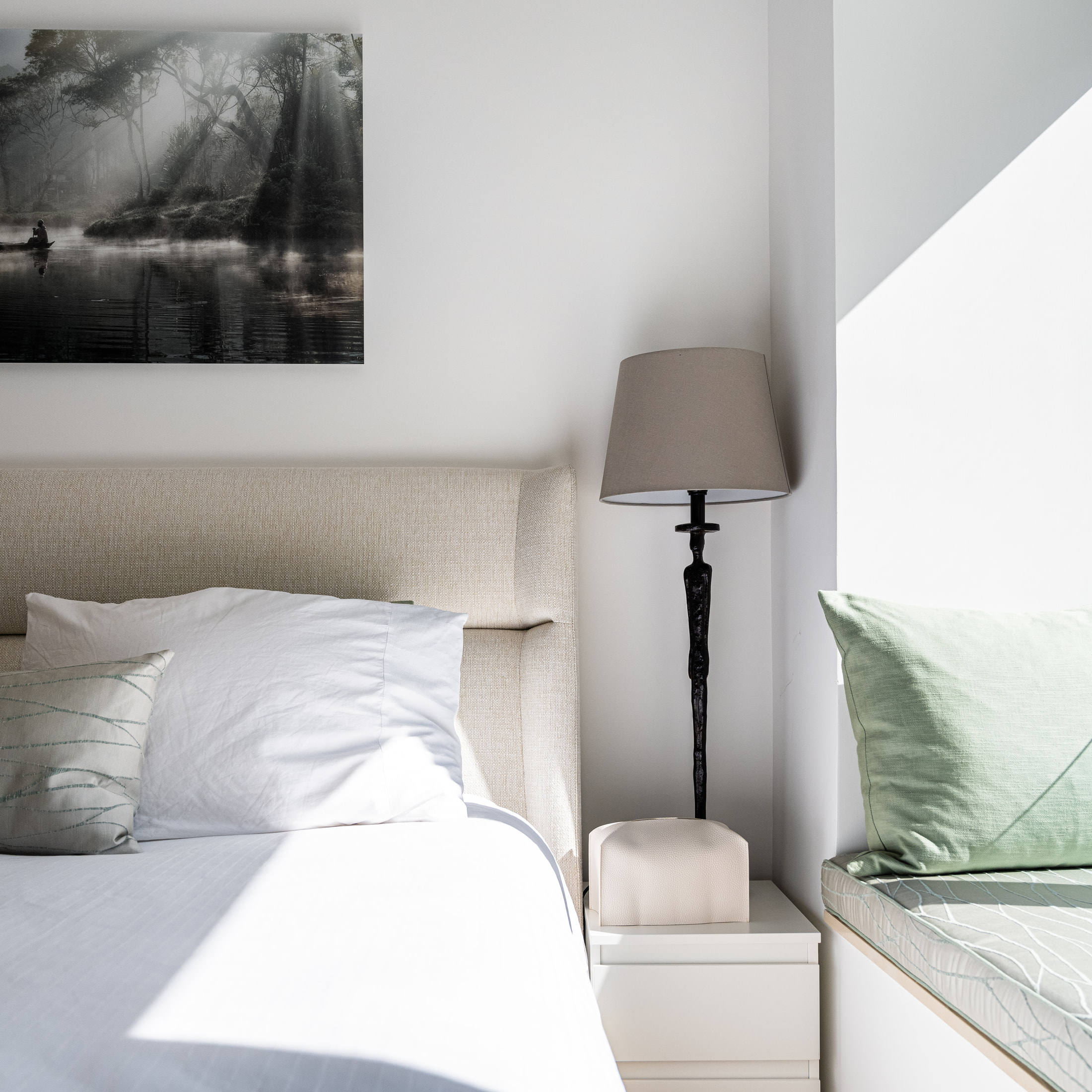 Bedside lamp, framed photograph and pale green cushions on the bedroom window seat